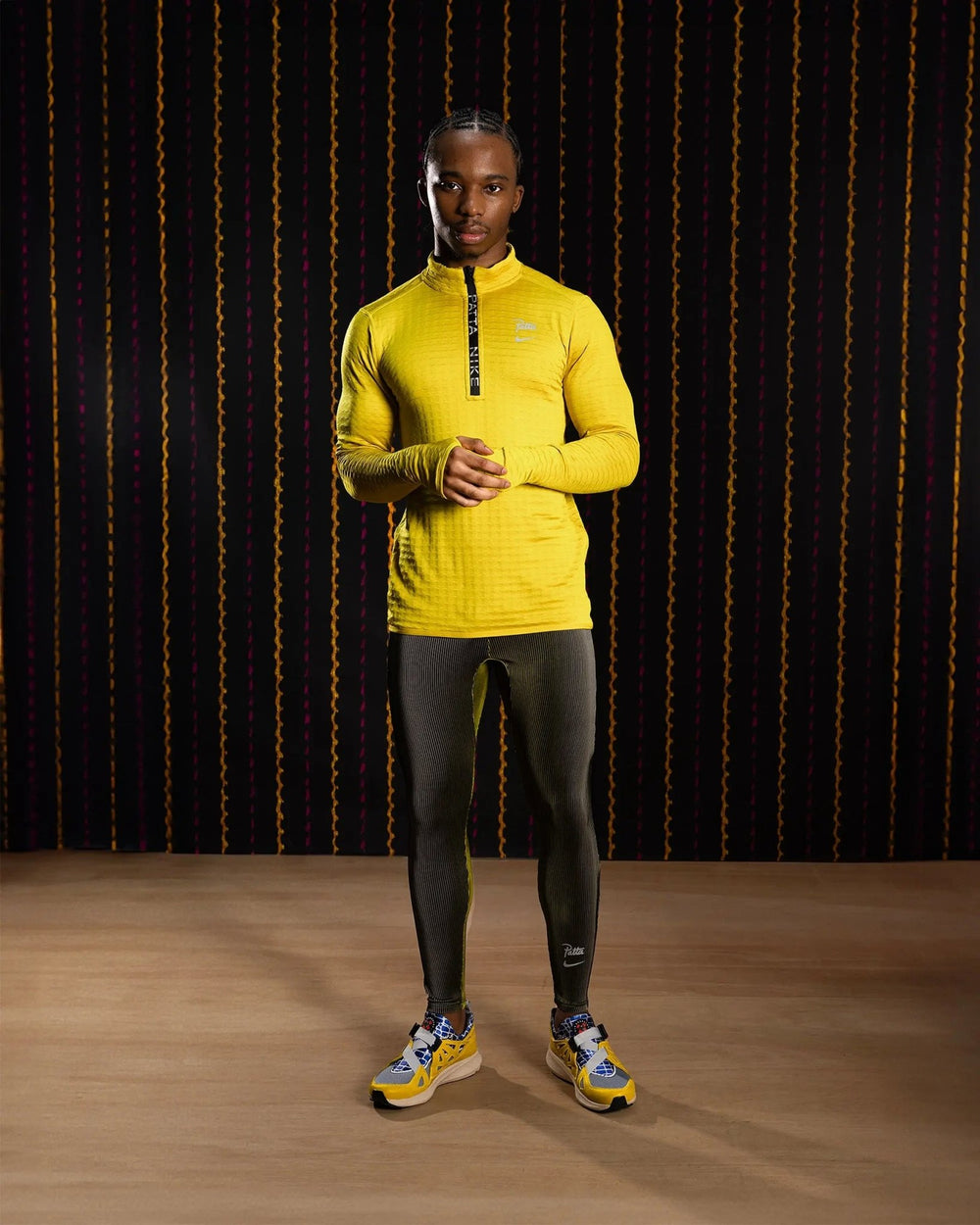 Male model wearing Nike x Patta Running Team leggings in Saffron Quartz with reflective details.