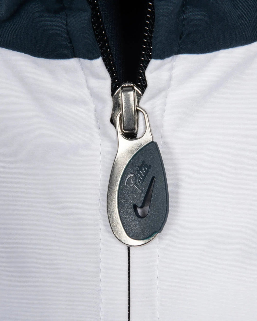 Custom Patta x Nike metal zipper puller detail on the Deep Ocean and white NRG track jacket.